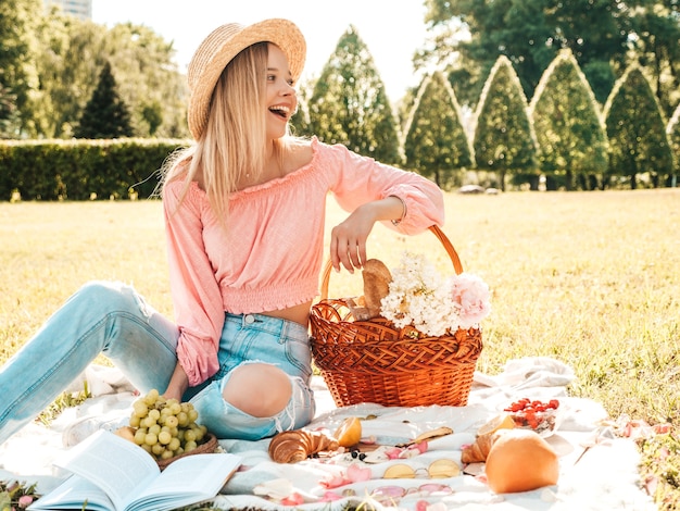 Young beautiful hipster woman in trendy summer jeans, pink T-shirt and hat. Carefree woman making picnic outside. 