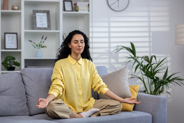 Young beautiful hispanic woman alone at home meditating sitting on sofa in lotus position woman with