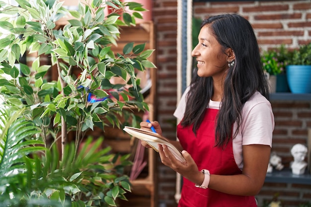 Young beautiful hispanic woman florist smiling confident writing on notebook at flower shop