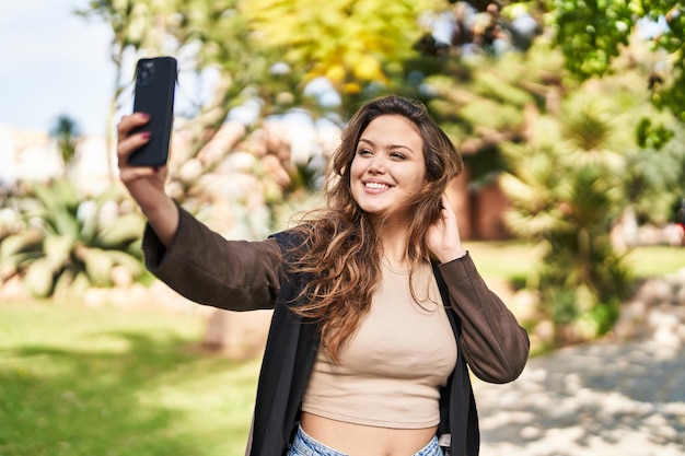 Young beautiful hispanic woman smiling confident making selfie by the smartphone at park