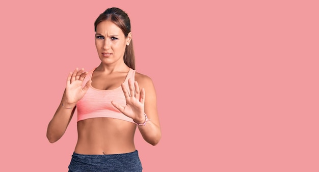 Young beautiful hispanic woman wearing sportswear afraid and terrified with fear expression stop gesture with hands shouting in shock panic concept