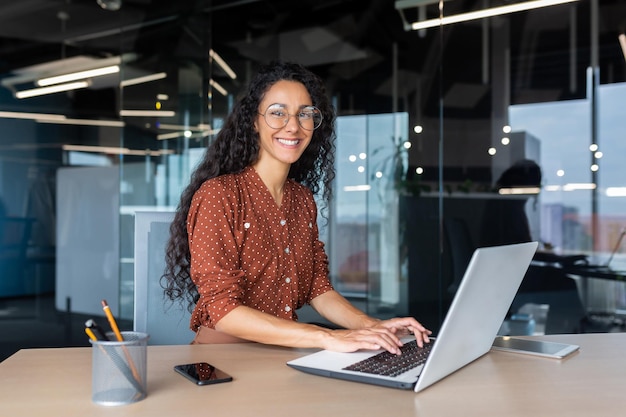 Young beautiful hispanic woman working inside modern office businesswoman smiling and looking at