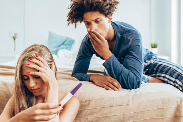 Young beautiful interracial couple in bed unhappy with pregnancy