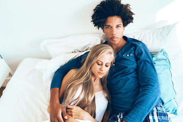 Young beautiful interracial couple relaxed lying down in bed cuddling