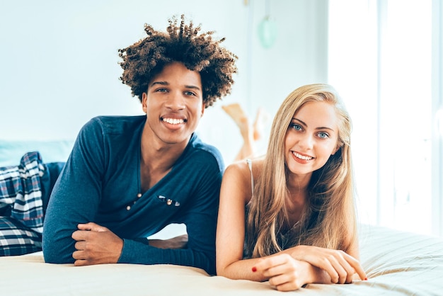 Young beautiful interracial couple relaxed lying down in bed cuddling