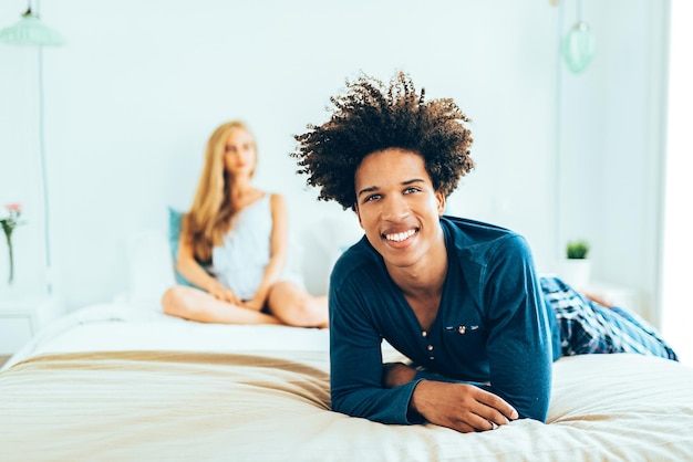 Young beautiful interracial couple relaxed lying down in bed cuddling