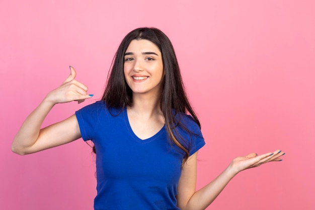 Young beautiful ladies standing on pink background and gesture call me