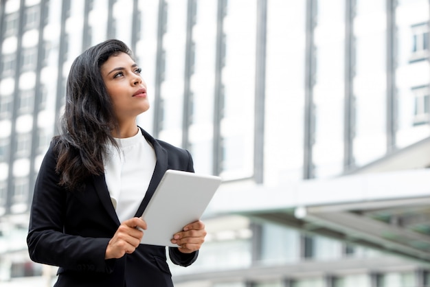 Young beautiful Latin business woman holding tablet computer and thinking