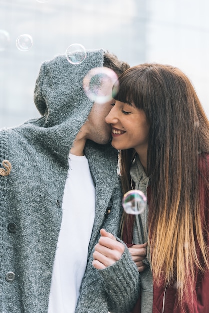 Young beautiful in love couple hugging each other in the middle of the street in a romantic way with soap bubbles 
