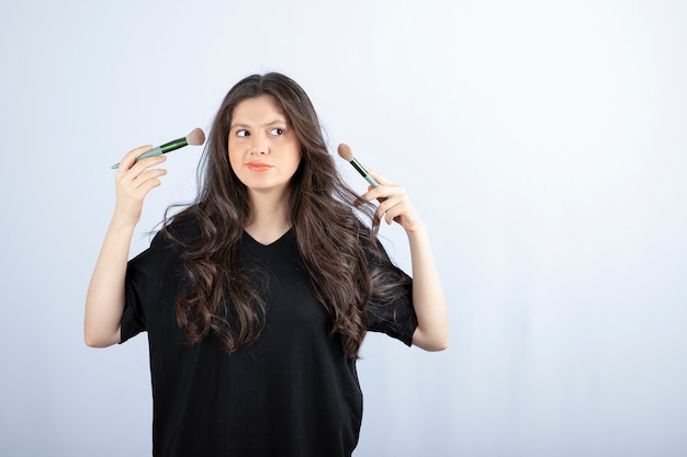 Young beautiful model with brush looking on white.