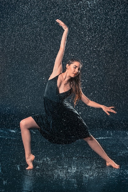 The young beautiful modern dancer dancing under water drops in blue aqua studio