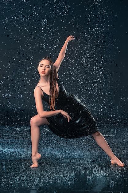 The young beautiful modern dancer dancing under water drops in blue aqua studio