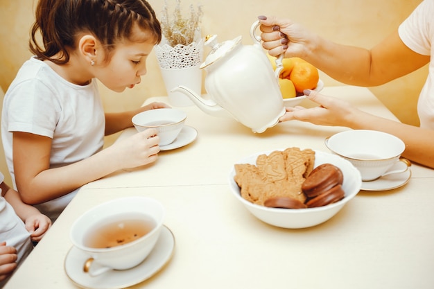 Young and beautiful mom in the kitchen with her children drinking tea with cookies