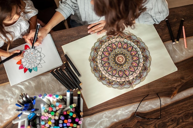 Photo young beautiful mother and cute daughter draw a mandala pattern together artistic markers and colore...