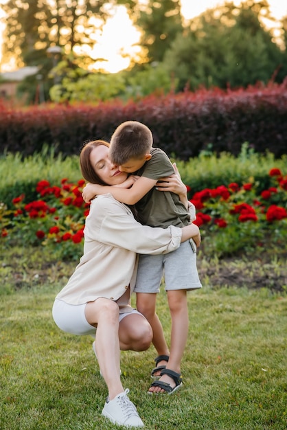 A young beautiful mother kisses and hugs her little son during the sunset in the park. Happy family walk in the park.