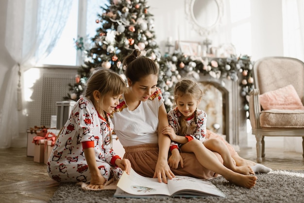 Young beautiful mother with two little daughters sit on the carpet and read book