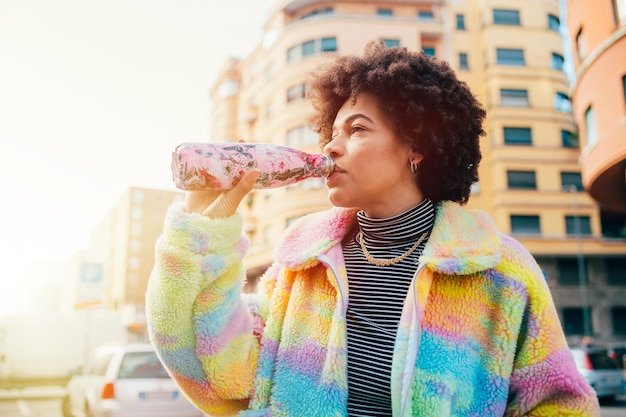 Young beautiful multiethnic woman drinking from reusable stainless bottle