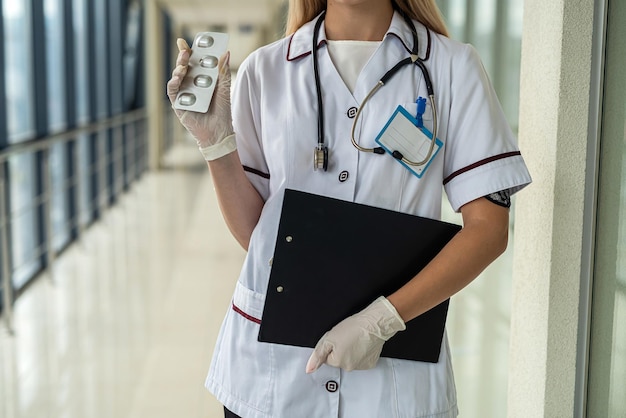 Young beautiful nurse stands in the hallway in uniform mask gloves stethoscope and holds a tablet