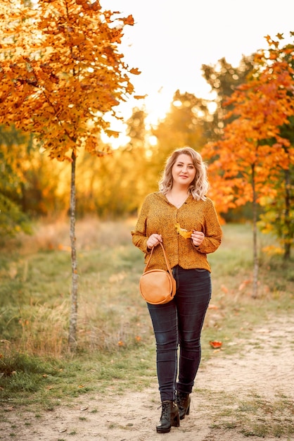 Young beautiful plussize woman in an orange shirt and jeans walks in an autumn park