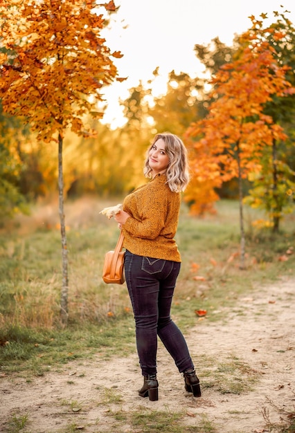 Young beautiful plussize woman in an orange shirt and jeans walks in an autumn park