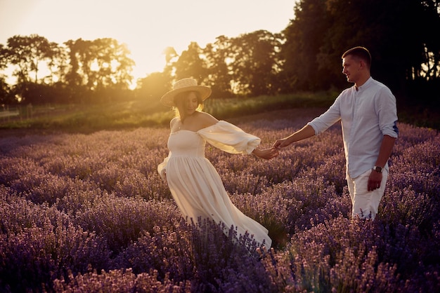 Young beautiful pregnant couple walking on a lavender field at sunset Happy family concept