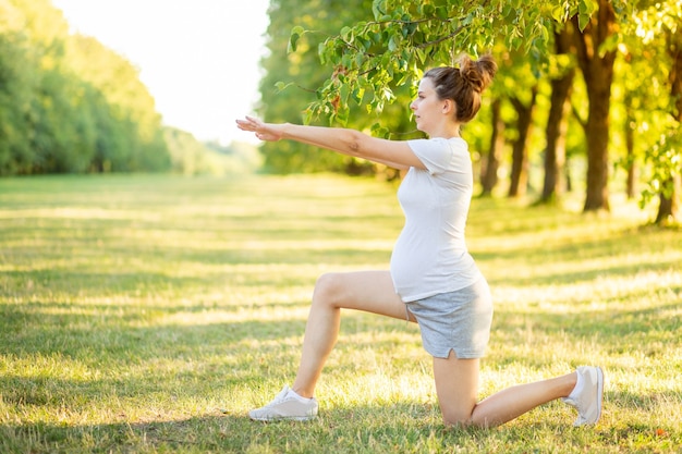 Young beautiful pregnant girl sitting on the green grass