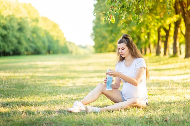 Young beautiful pregnant girl sitting on the green grass