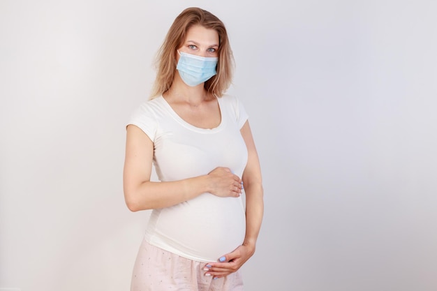 Young beautiful pregnant woman in medical surgical mask and white tshirt quarantined isolation stay at home