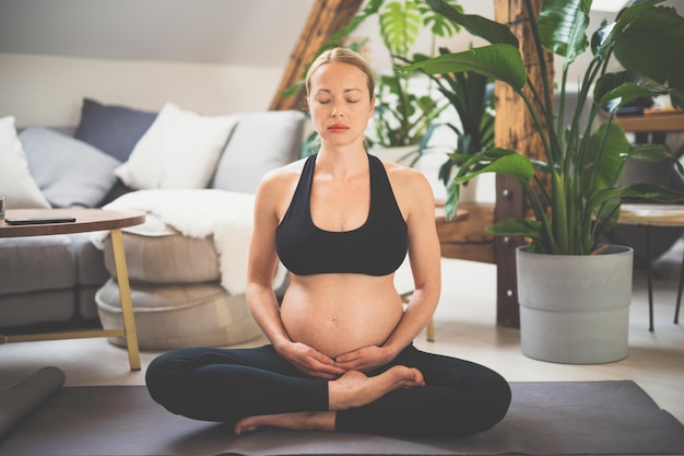 Young beautiful pregnant woman training yoga caressing her belly Young happy expectant relaxing thinking about her baby and enjoying her future life Motherhood pregnancy yoga concept