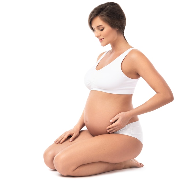 Young and beautiful pregnant woman on white wall