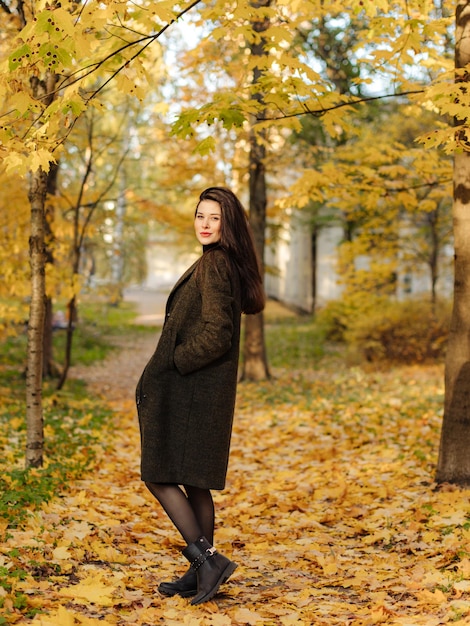 Young beautiful pregnant woman with dark hair in a black tight dress and coat posing