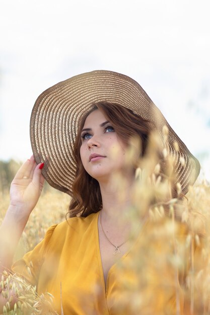 A young beautiful pregnant woman in a yellow dress and hat walks through a wheat orange field on a sunny summer day