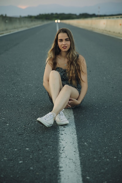 Young beautiful rebel woman on empty road at sunset