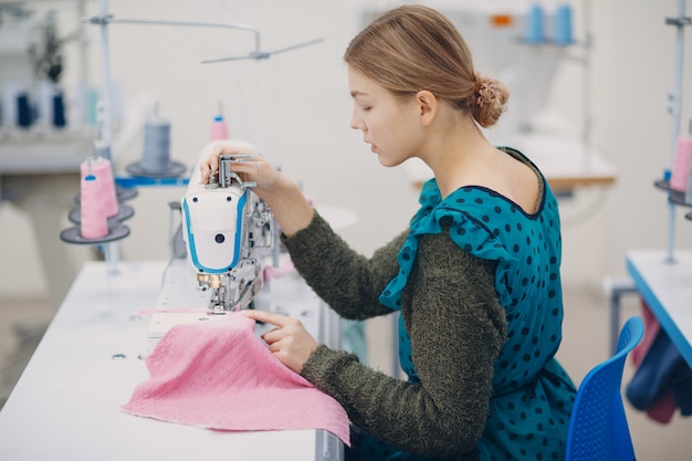 Young beautiful seamstress sews on sewing machine in fabric factory