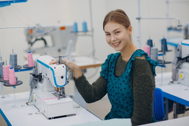 Young beautiful seamstress sews on sewing machine in factory.