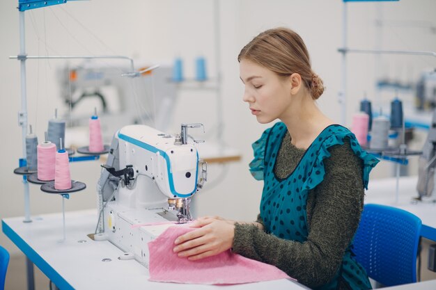 Young beautiful seamstress sews on sewing machine in factory