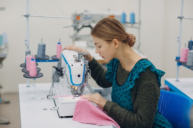 Young beautiful seamstress sews on sewing machine in factory