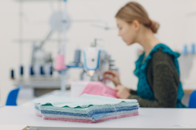 Young beautiful seamstress sews on sewing machine in factory