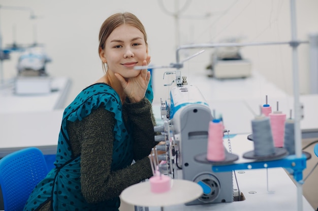 Young beautiful seamstress sews on sewing machine in factory