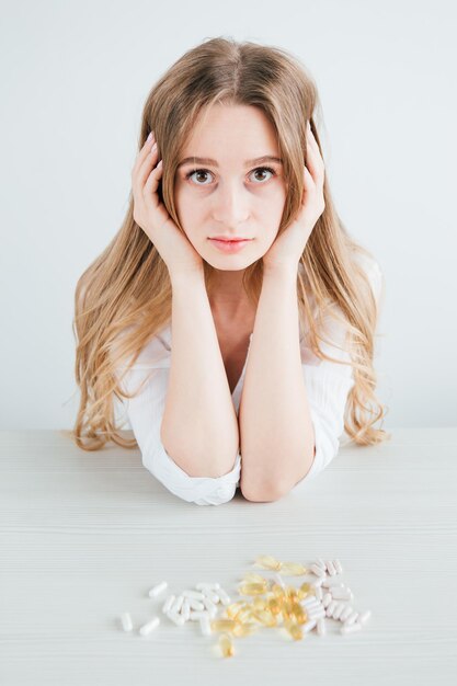 Young beautiful sick girl chooses pills. Colorful capsules of tablets, vitamins, dietary supplements are on the table. Toning.