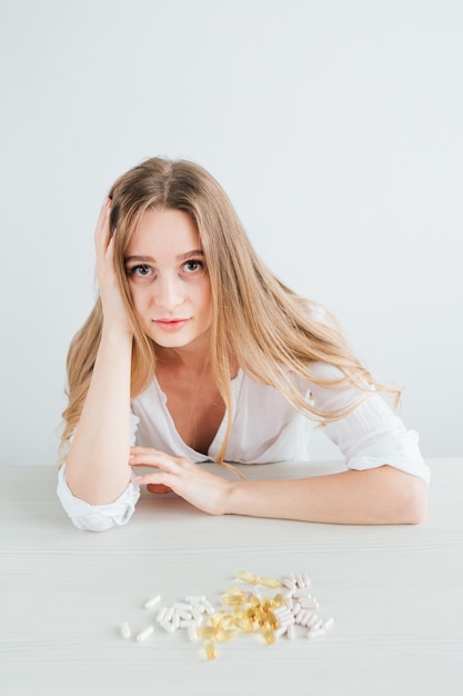 Young beautiful sick girl chooses pills. Colorful capsules of tablets, vitamins, dietary supplements are on the table. Toning.