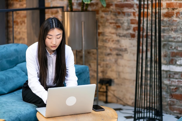 Young beautiful smiling asian business girl working on laptop housed at wooden table in office