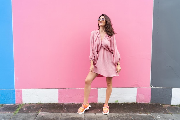 Young beautiful smiling cute romantic woman in trendy summer dress Carefree woman posing in the street near pink wall Positive model outdoors in sunglasses Cheerful and happyxA