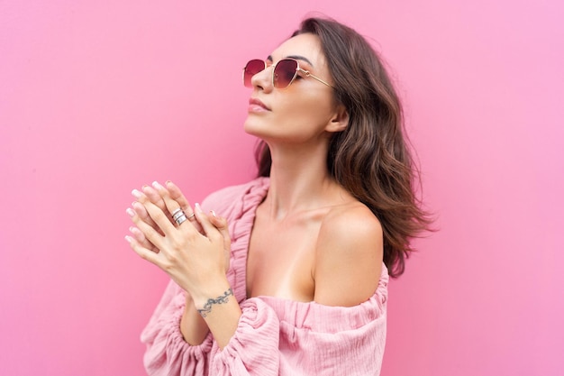 Young beautiful smiling cute romantic woman in trendy summer dress Carefree woman posing in the street near pink wall Positive model outdoors in sunglasses Cheerful and happyxA