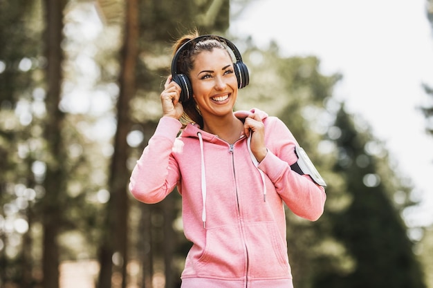 Young beautiful smiling female runner listening to music and preparing to jogging in nature.