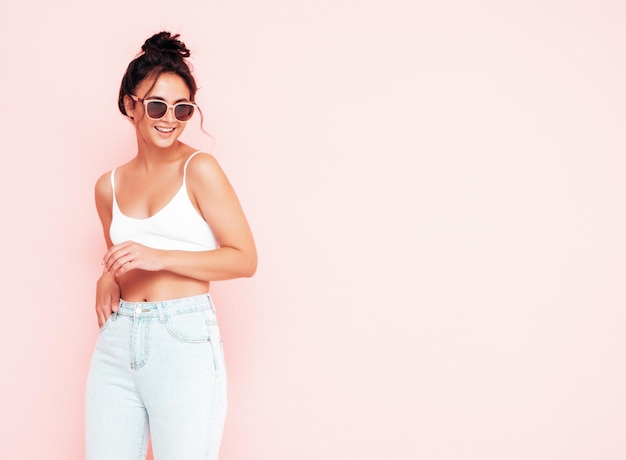 Young beautiful smiling female in trendy summer clothes Sexy carefree woman posing near pink wall in studio Positive brunette model having fun and going crazy Cheerful and happy