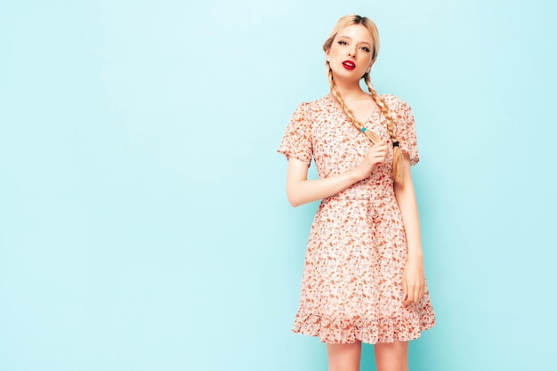 Young beautiful smiling female in trendy summer dress Sexy carefree blond woman posing near blue wall in studio Model having fun Cheerful and happy