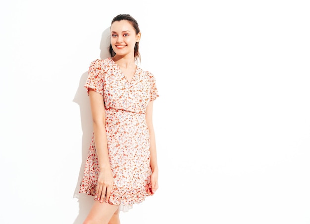 Young beautiful smiling female in trendy summer dress Sexy carefree woman posing near red wall in studio Positive brunette model having fun and going crazy Cheerful and happy