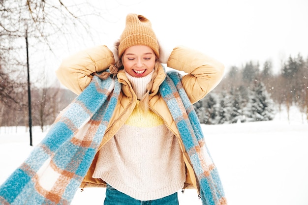 Young beautiful smiling hipster female in trendy warm clothes and scarf.Carefree woman posing in the street in park. Positive pure model having fun in snow. Enjoying winter moments