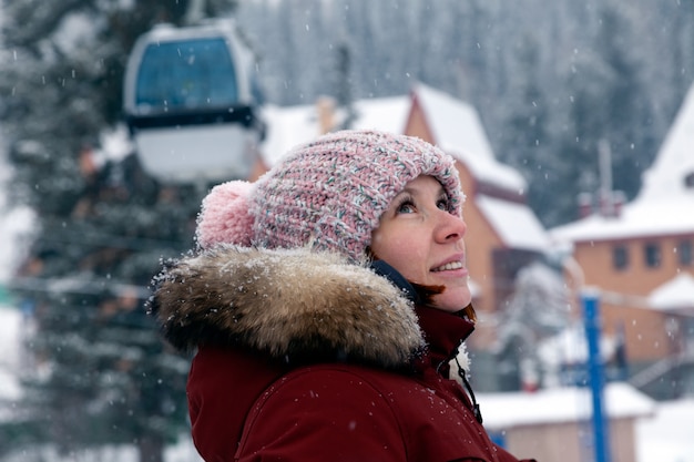 Young beautiful smiling woman looking sideways in pink knitted hat with pompon in warm jacket outdoors